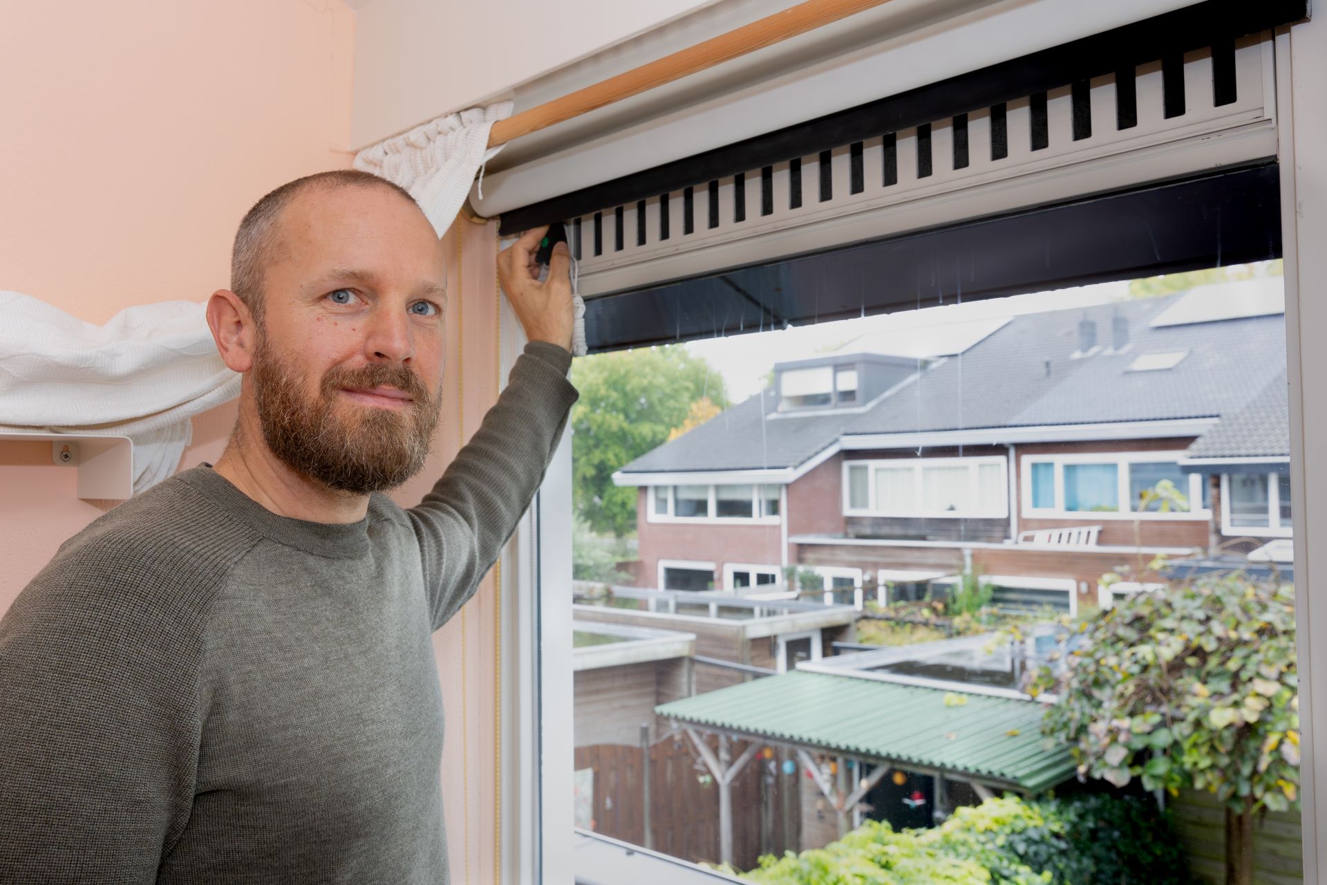 Een man staat bij het ventilatierooster van een raam.