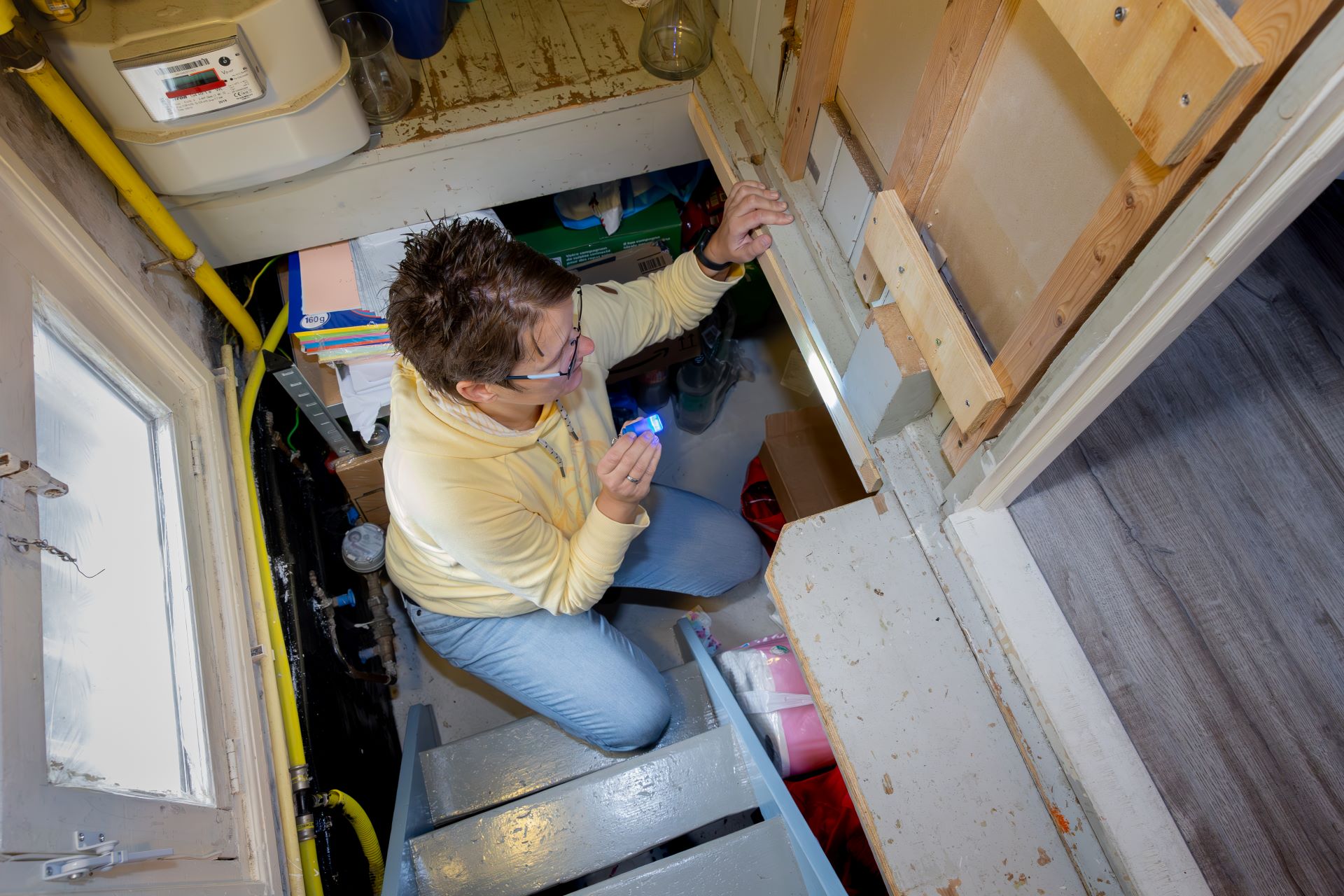 Een dame zit in een kruipruimte en bekijkt met een zaklamp de isolatie